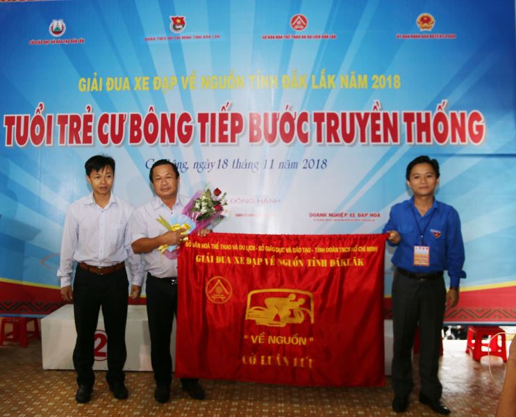 Đại diện huyện Krông Bông (đứng giữa) nhận cờ đơn vị đăng cai Giải đua xe đạp “Về nguồn” tỉnh Đắk Lắk lần thứ XXIV năm 2019.
